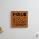 Brown leatherette wall sign engraved with a Michigan design of a lighthouse, a whitetail buck and both peninsulas, hanging on a wall
