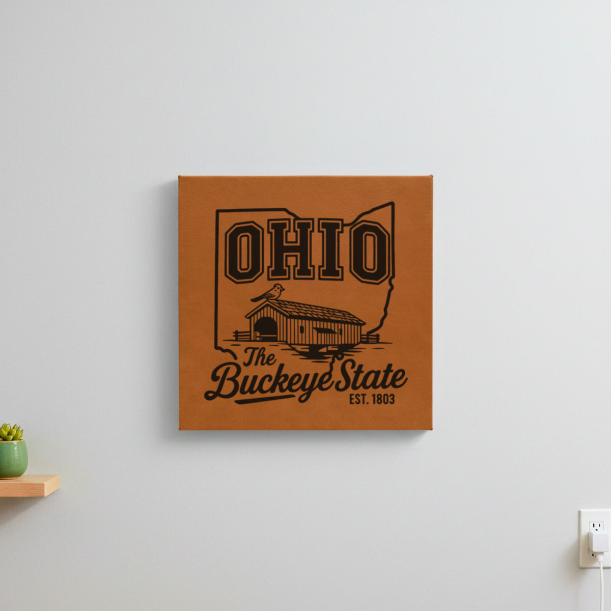 Brown leatherette wall sign engraved with an Ohio design of a covered bridge and a cardinal, hanging on a wall