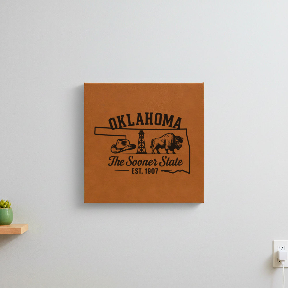 Brown leatherette wall sign engraved with an Oklahoma design of a cowboy hat, an oil derrick and a bison, hanging on a wall