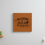 Brown leatherette wall sign engraved with an Oklahoma design of a cowboy hat, an oil derrick and a bison, hanging on a wall