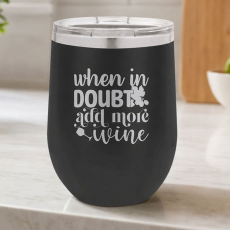 Black 12 oz stemless wine tumbler laser engraved with "When in Doubt, Add More Wine", on a kitchen counter