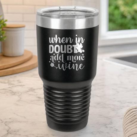 Black 30 oz tumbler laser engraved with "When in Doubt, Add More Wine", on a kitchen counter
