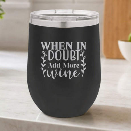 Black 12 oz stemless wine tumbler laser engraved with "When in Doubt, Add More Wine", on a kitchen counter