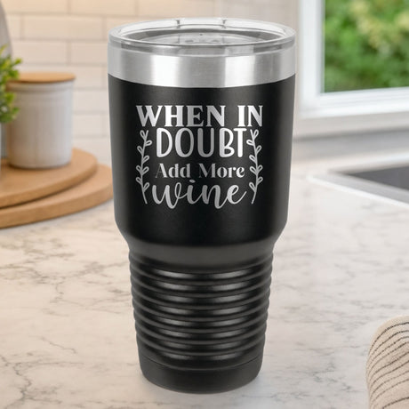 Black 30 oz tumbler laser engraved with "When in Doubt, Add More Wine", on a kitchen counter