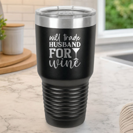 Black 30 oz tumbler laser engraved with "Will Trade Husband for Wine", on a kitchen counter