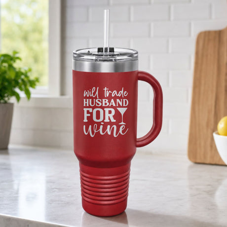 Maroon 40 oz tumbler with handle and straw laser engraved with "Will Trade Husband for Wine", on a kitchen counter