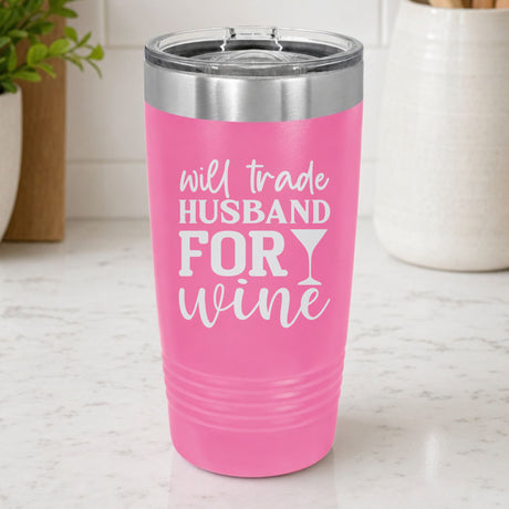 Pink 20 oz tumbler laser engraved with "Will Trade Husband for Wine", on a kitchen counter
