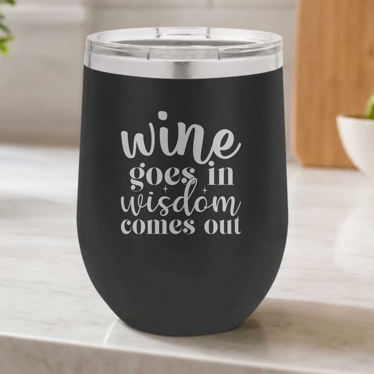 Black 12 oz stemless wine tumbler laser engraved with "Wine Goes In, Wisdom Comes Out", on a kitchen counter