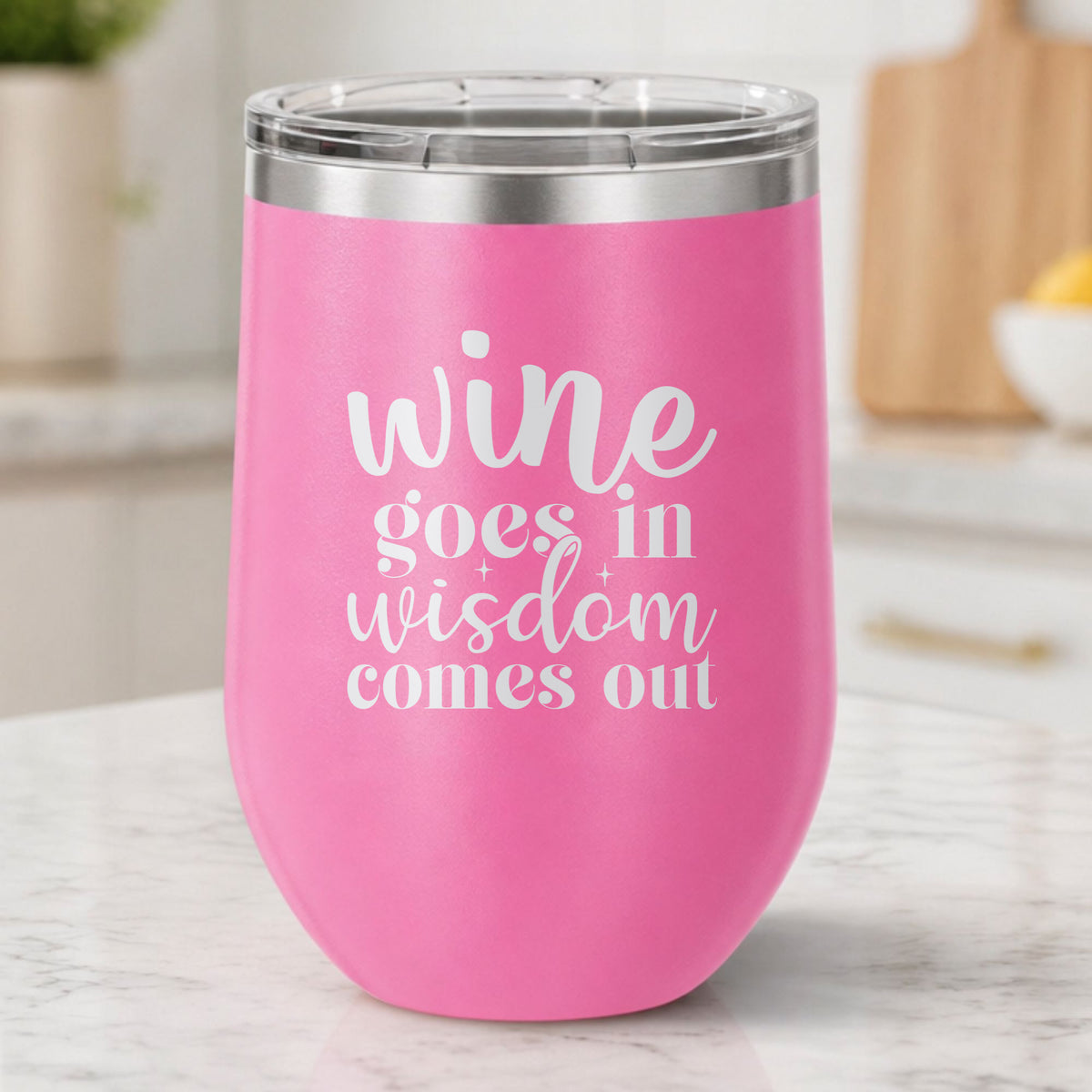 Pink 12 oz stemless wine tumbler laser engraved with "Wine Goes In, Wisdom Comes Out", on a kitchen counter