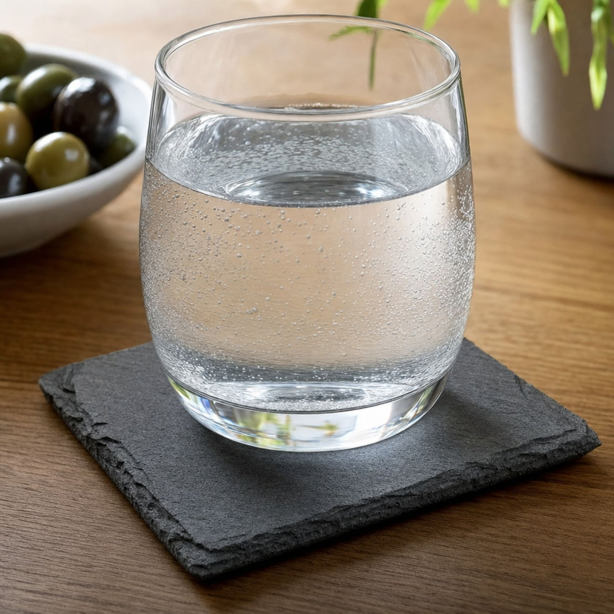 Square slate coaster on a wood table holding a glass of sparkling water
